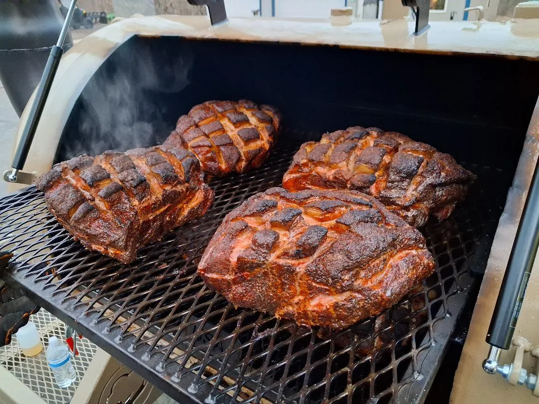 Scored pork butts smoking inside the offset smoker